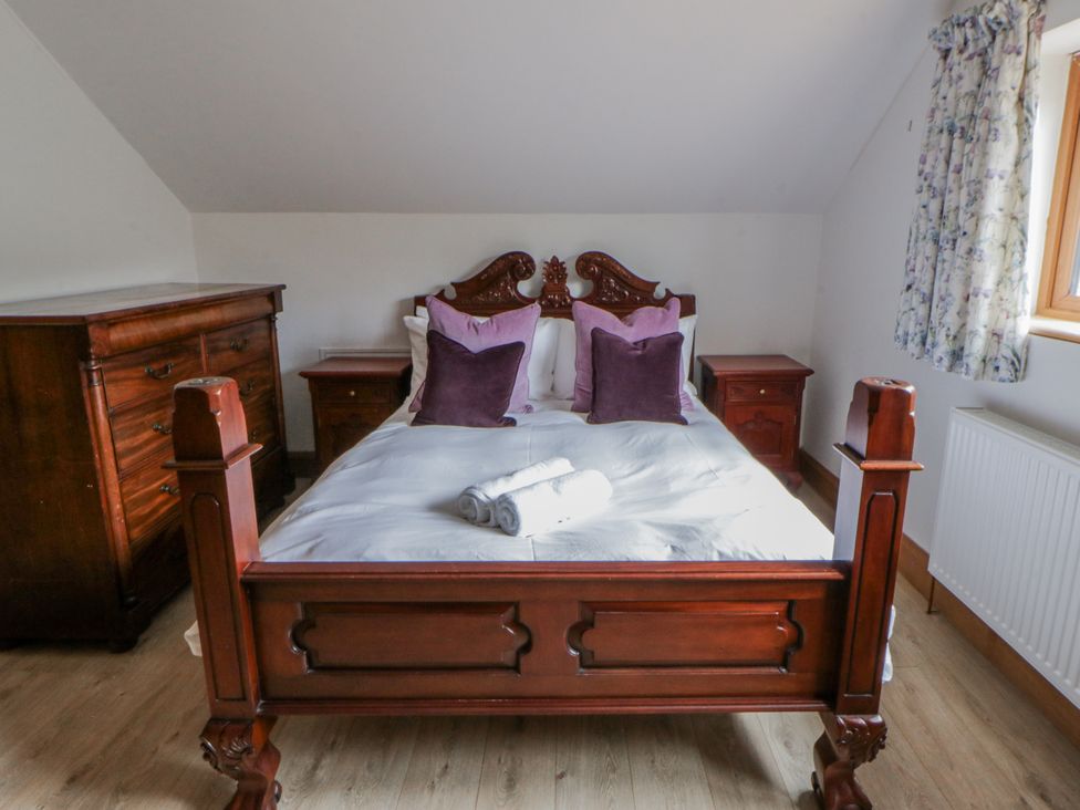 A bedroom with a wooden bed, pillows, and furniture at Ty-Gan Dderwen in Llangennech