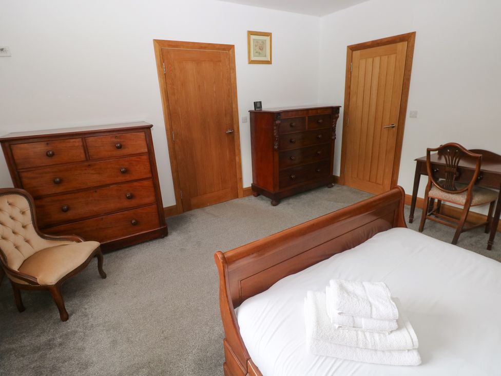 A bedroom with a bed, dresser, table and chair at Ty-Gan Dderwen in Llangennech, Llanelli