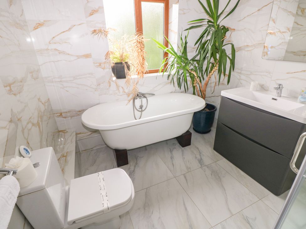 A bathroom with a bathtub, toilet, sink, and plant at Ty-Gan Dderwen, Llangennech, Llanelli