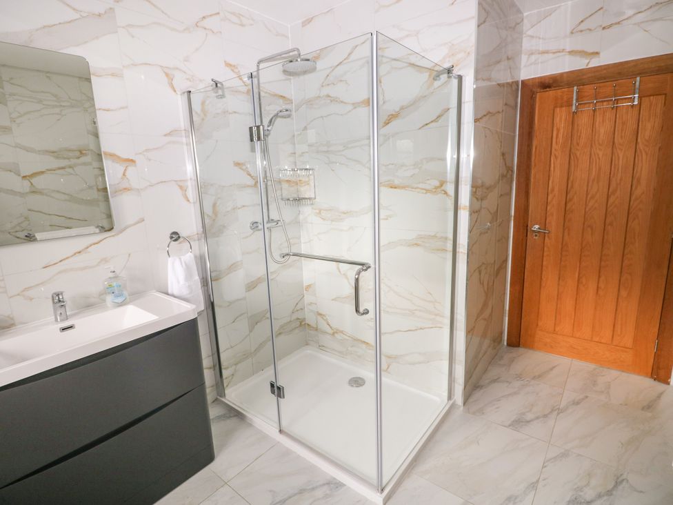 A bathroom with a shower, mirror, and sink at Ty-Gan Dderwen, Llangennech, Llanelli