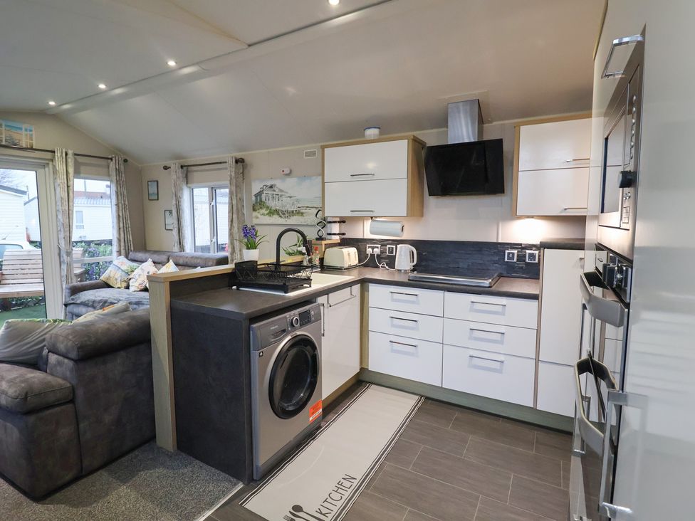 A kitchen with a washing machine and sofa at Offspray Court 1 in Scratby