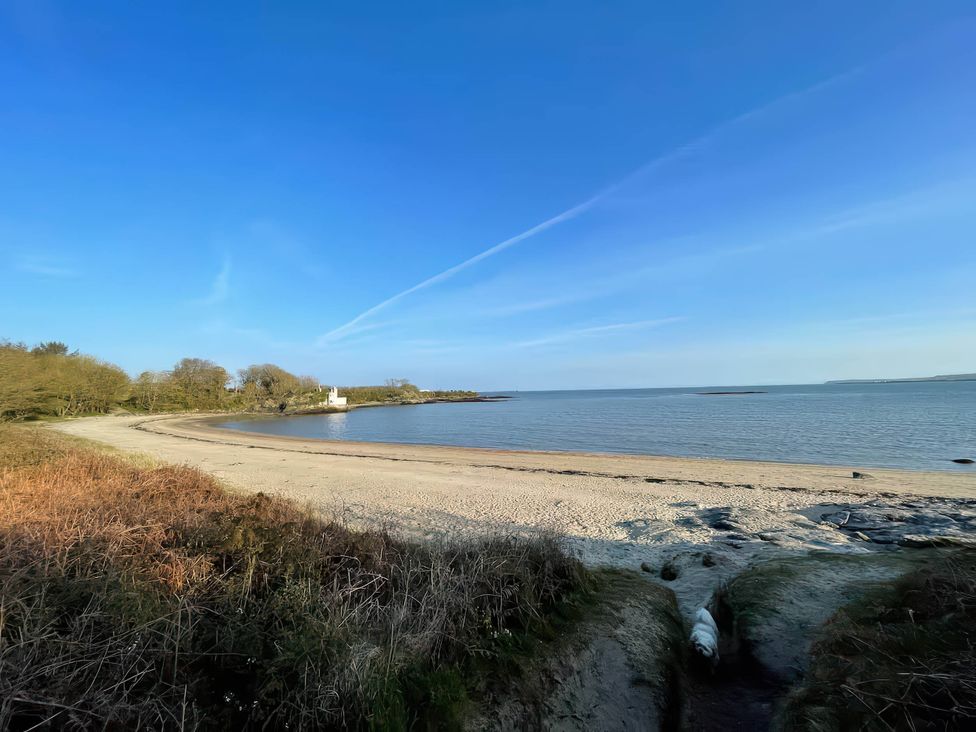 A beach with water and trees at Swan Cottage in Llangaffo