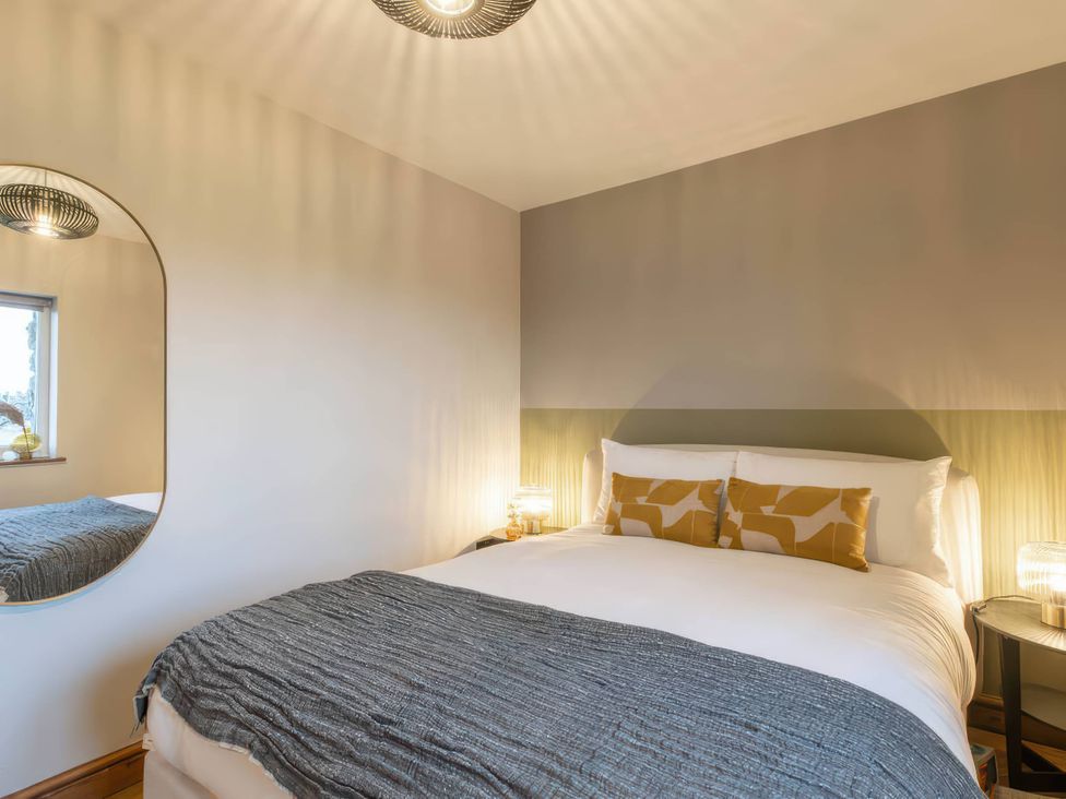 A bedroom with a bed and mirror at Blue Bird Cottage in Llangaffo