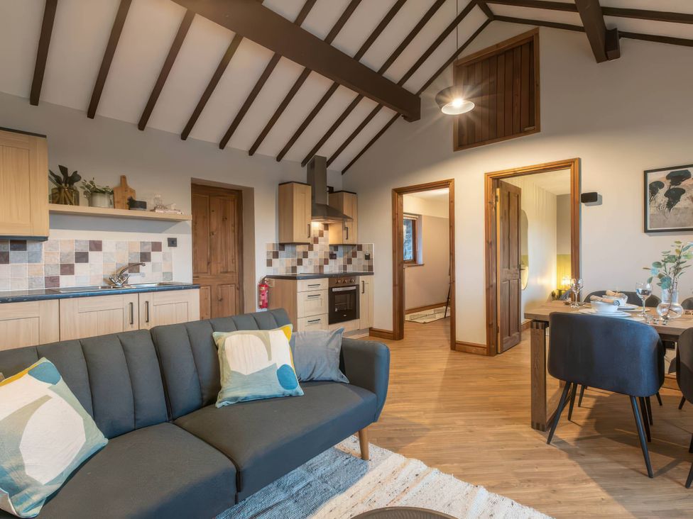 A living room with a sofa, table, and kitchen area at Blue Bird Cottage Llangaffo