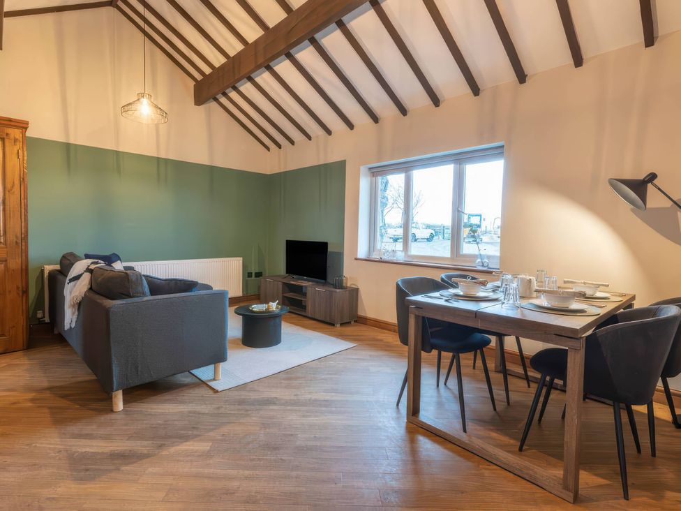A living room with a sofa, dining table, and television at Blue Bird Cottage Llangaffo