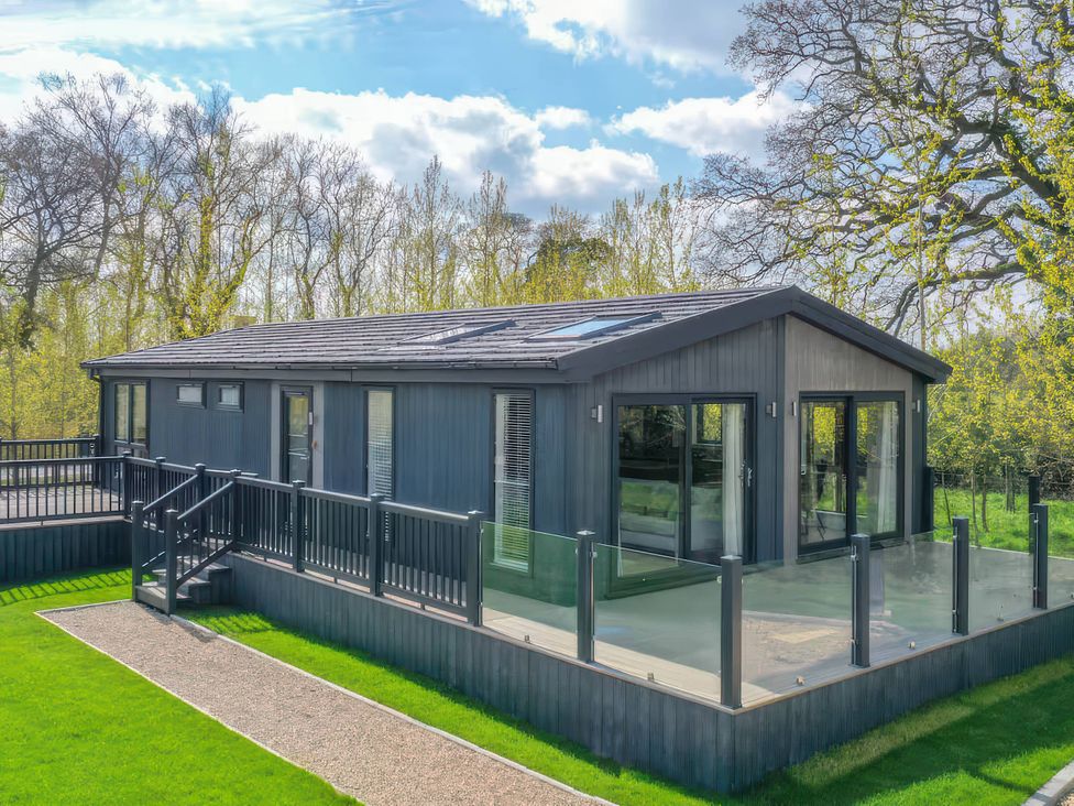 A lodge with a deck and glass railing at Isca Lodge - With Decking - Lodge 1 Wombleton