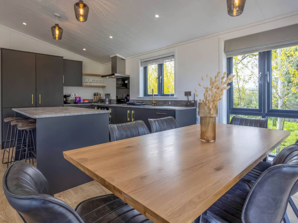 A kitchen with a dining table and bar stools at Isca Lodge - With Decking - Lodge 1 Wombleton