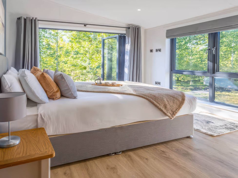 A bedroom with a bed and large windows at Isca Lodge - With Decking - Lodge 1, Wombleton