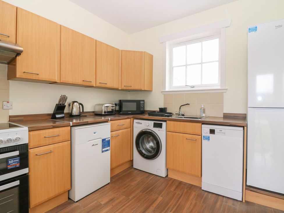A kitchen with appliances including oven, fridge, and washing machine at Bankhead Of Lour Bungalow