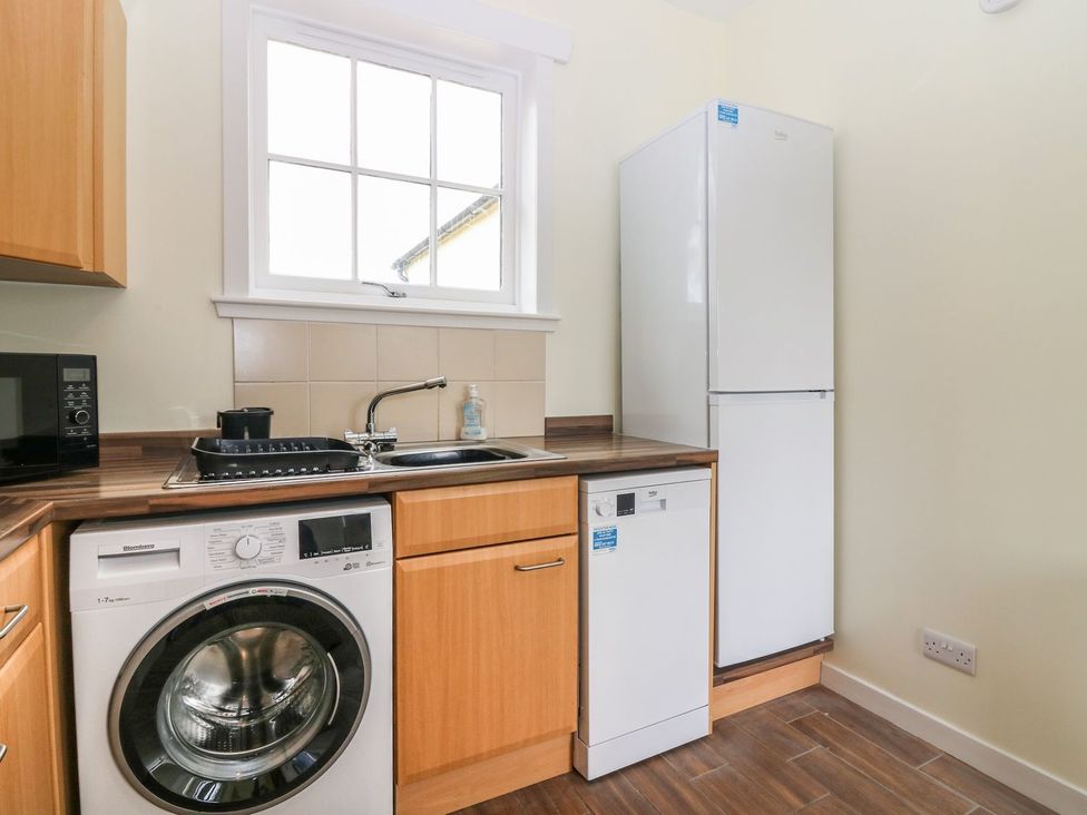 A kitchen with appliances including a washing machine, refrigerator, and microwave at Bankhead Of Lour Bungalow