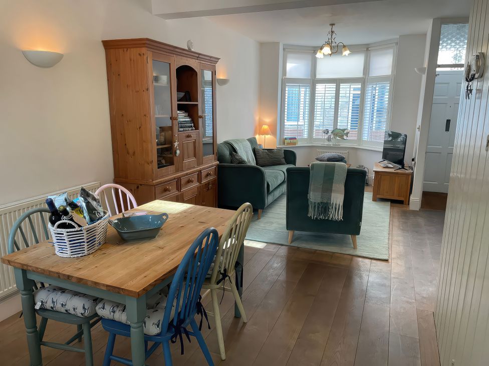 A dining area with a table and chairs beside a living area with a sofa and television at Seahorse Cottage in Weymouth