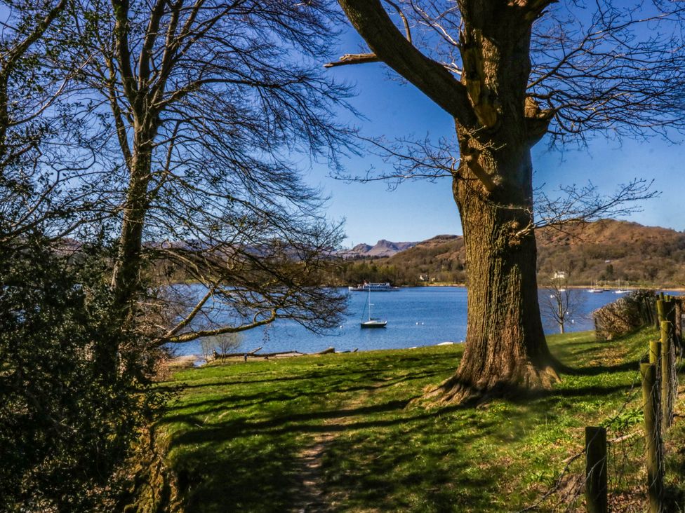 A view of a lake with a boat, trees, and a pathway at Terabitha Lodge in Troutbeck