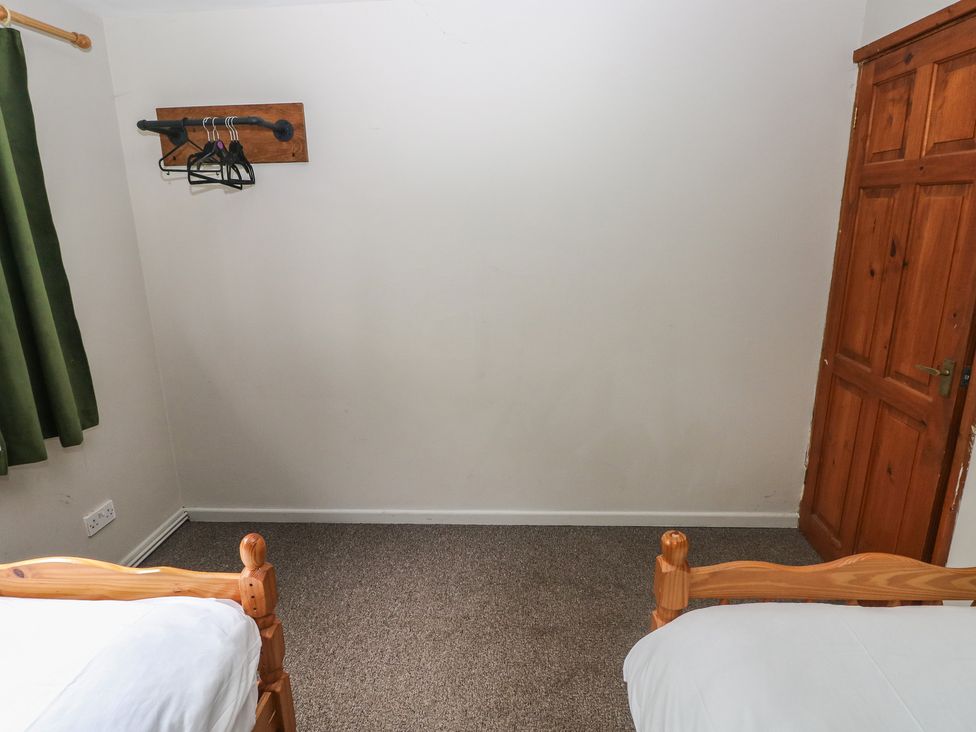 A bedroom with two beds, hangers on a wall, and a wooden door at Cabin No. 13 - Salt and Fern Cabins Goytre near Port Talbot