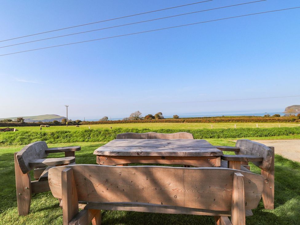 A table and benches in a grassy area near the ocean at Ty Felin in Newport