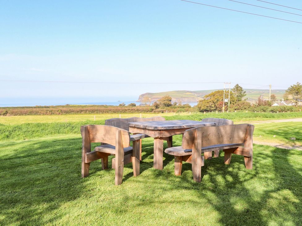 A table and benches on grass with a view of the ocean at Ty Felin Newport