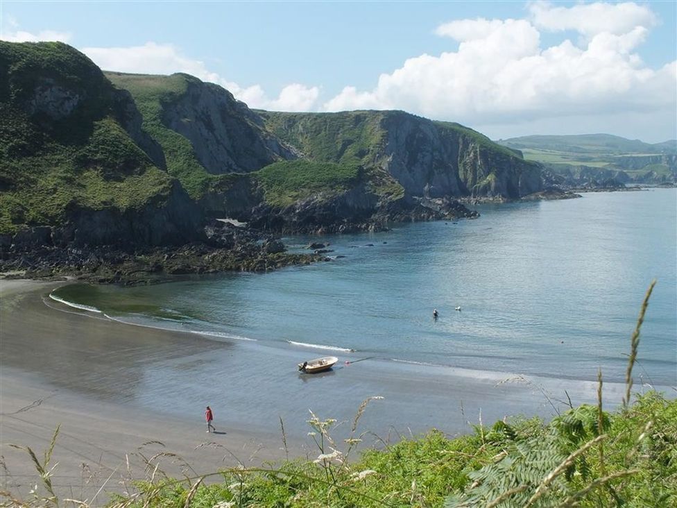 A beach with cliffs and a person walking at Dinas Island Cottage in Dinas Cross
