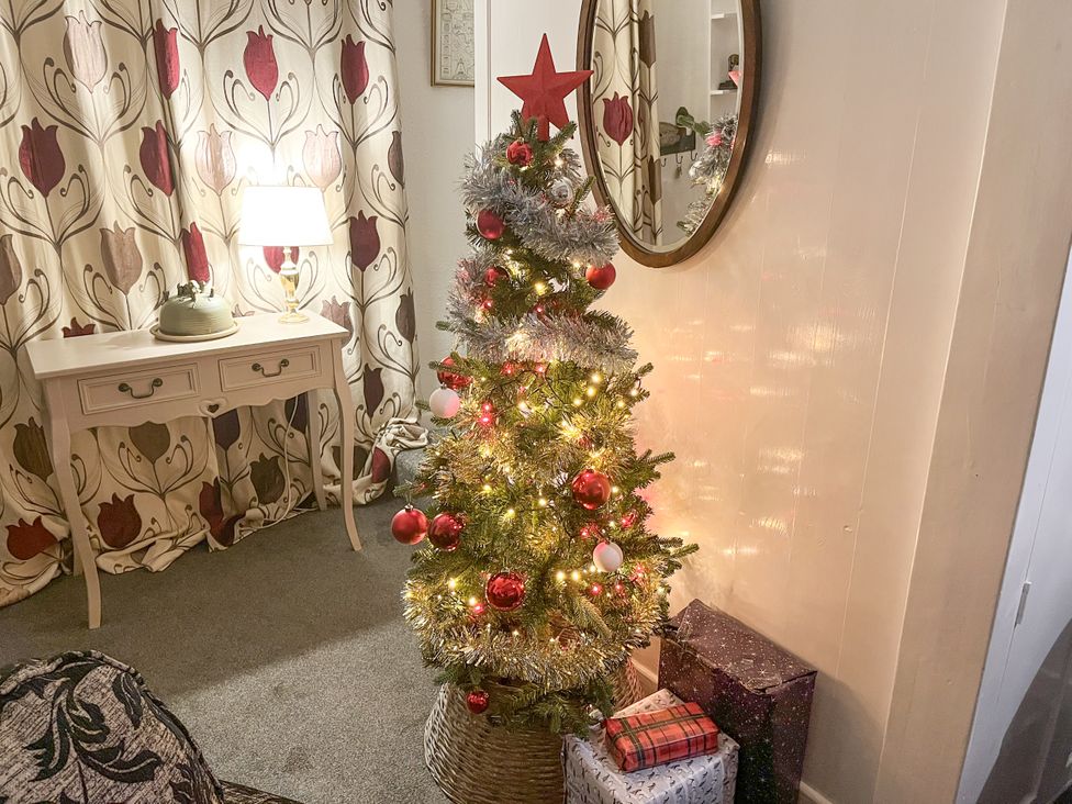 A Christmas tree with decorations and gifts in a living room at Bumble Bee at 2 Clematis Cottage near Clee Hill