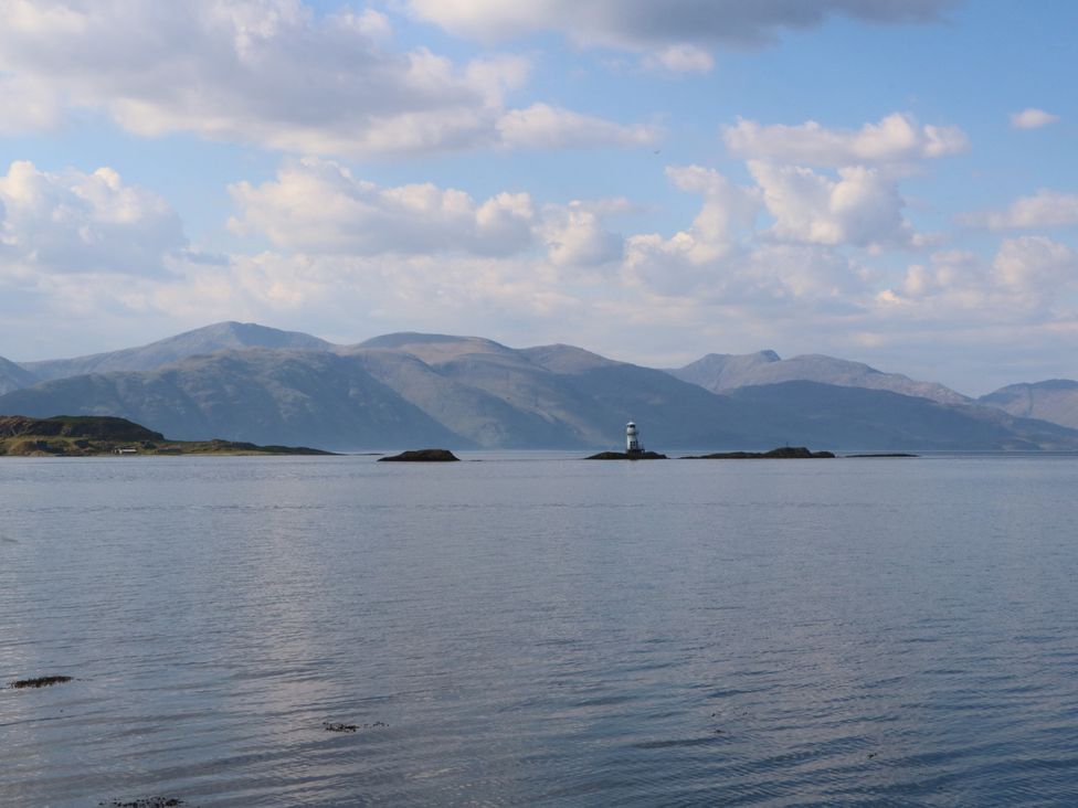 A lighthouse on an island with mountains in the background at Lurach House in Port Appin