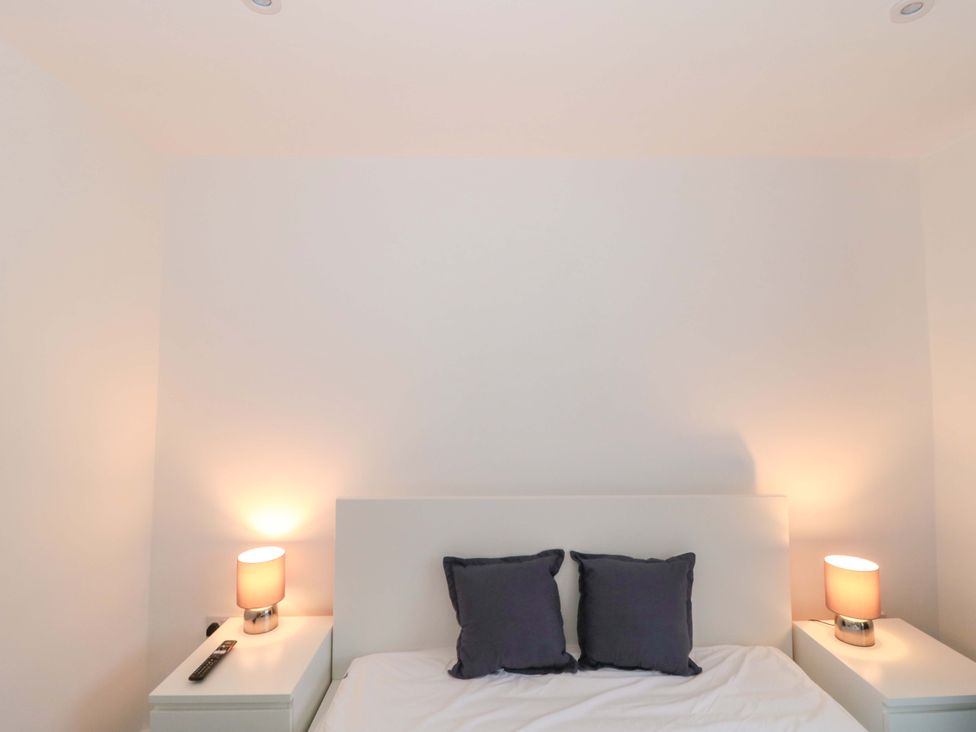 A bedroom with a bed, pillows, bedside lamps, and a remote control at 2 Stroud Bungalows