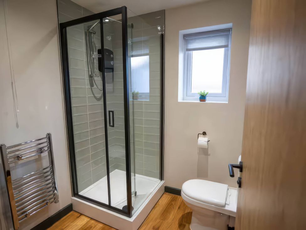 A bathroom with a shower, toilet, and towel rack at Ash Cottages in Llanrwst