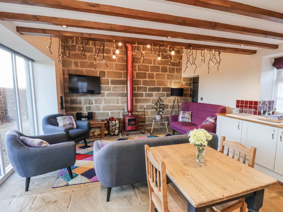 A living room with a sofa, armchairs, a wood stove and a dining table at Chestnut Barn Aislaby near Whitby