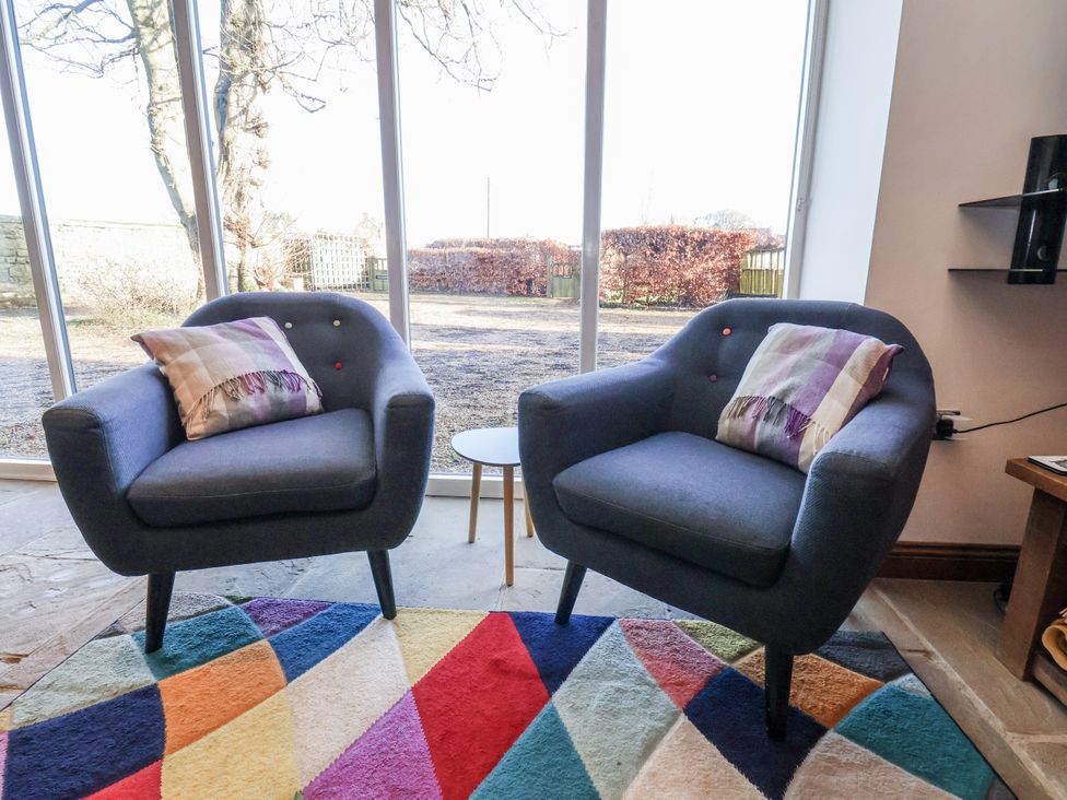 Two armchairs with cushions and a table in a living room at Chestnut Barn Aislaby near Whitby