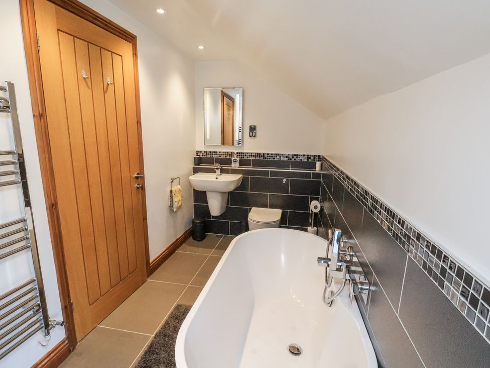 A bathroom with a bathtub, toilet, sink, and mirror at Chestnut Barn Aislaby near Whitby