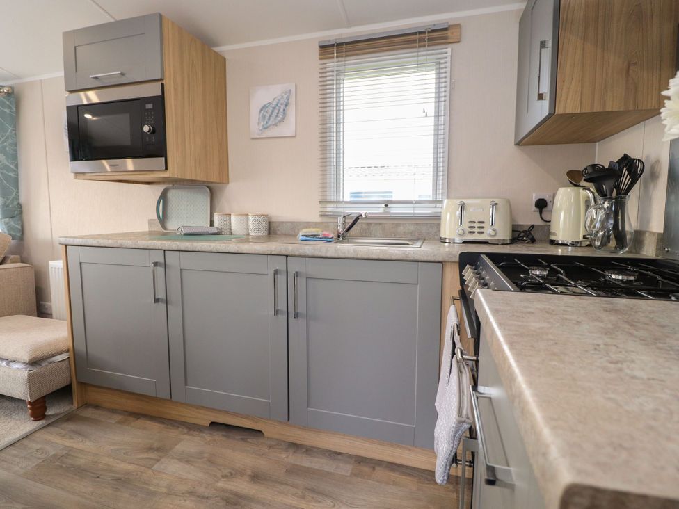 A kitchen with a microwave, sink, and cabinets at Poppy Lodge in Morecambe