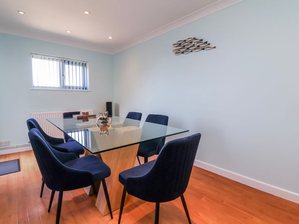 A dining room with a glass table and blue chairs at Sea Spray in Westward Ho!