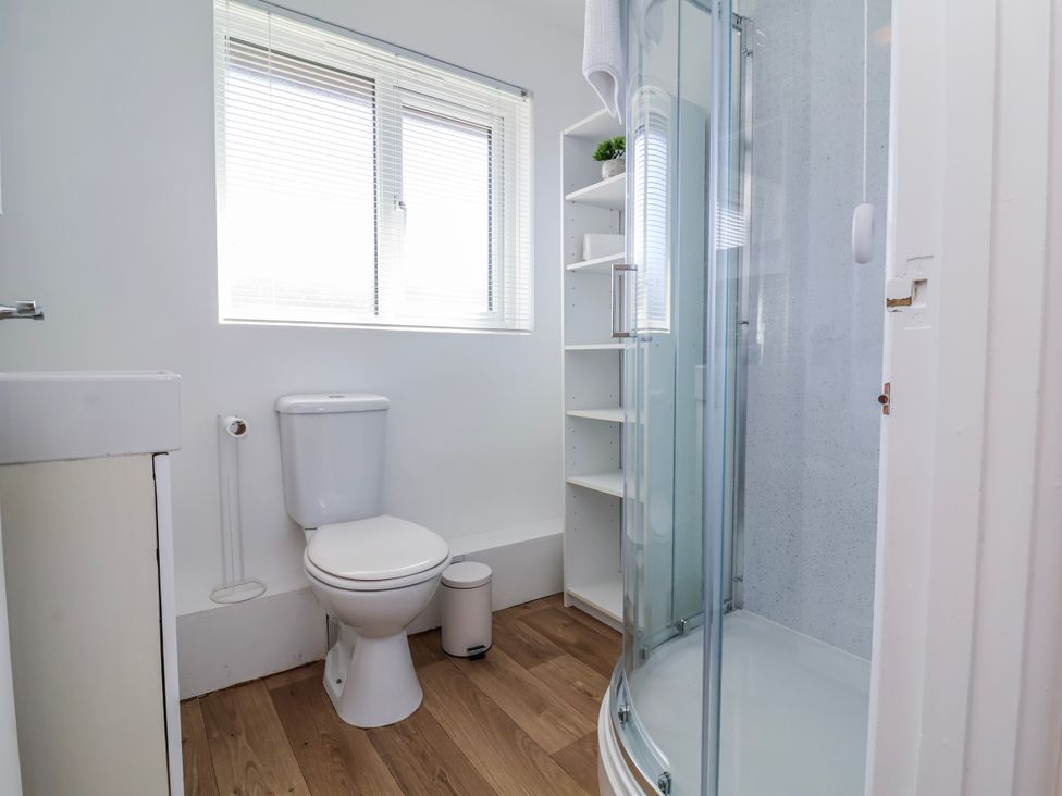 A bathroom with a shower, toilet, sink, and shelf at Sea Spray in Westward Ho!