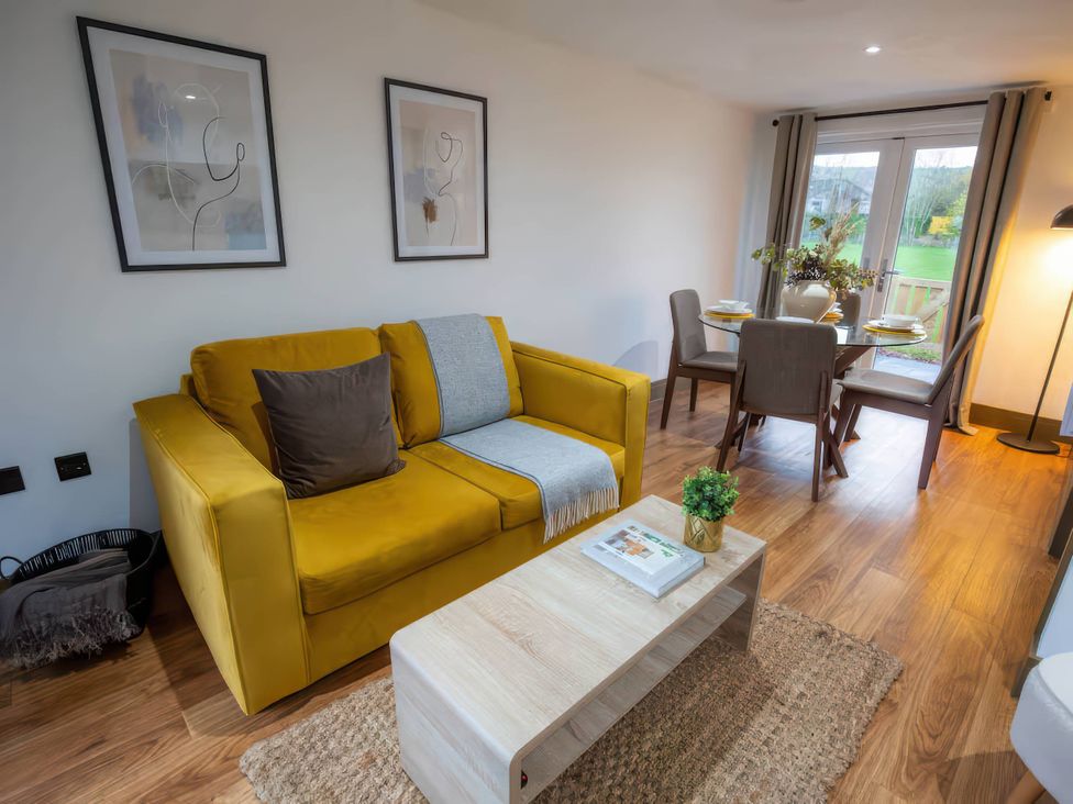 A living room with a yellow sofa and dining area at Fir Cottages in Llanrwst