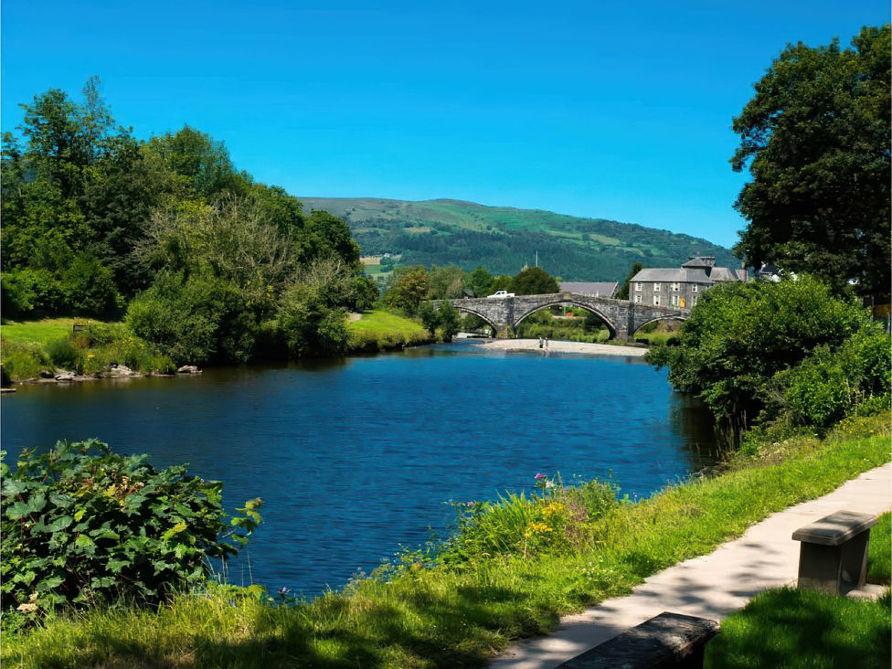 A river with a bridge and trees at Fir Cottages in Llanrwst