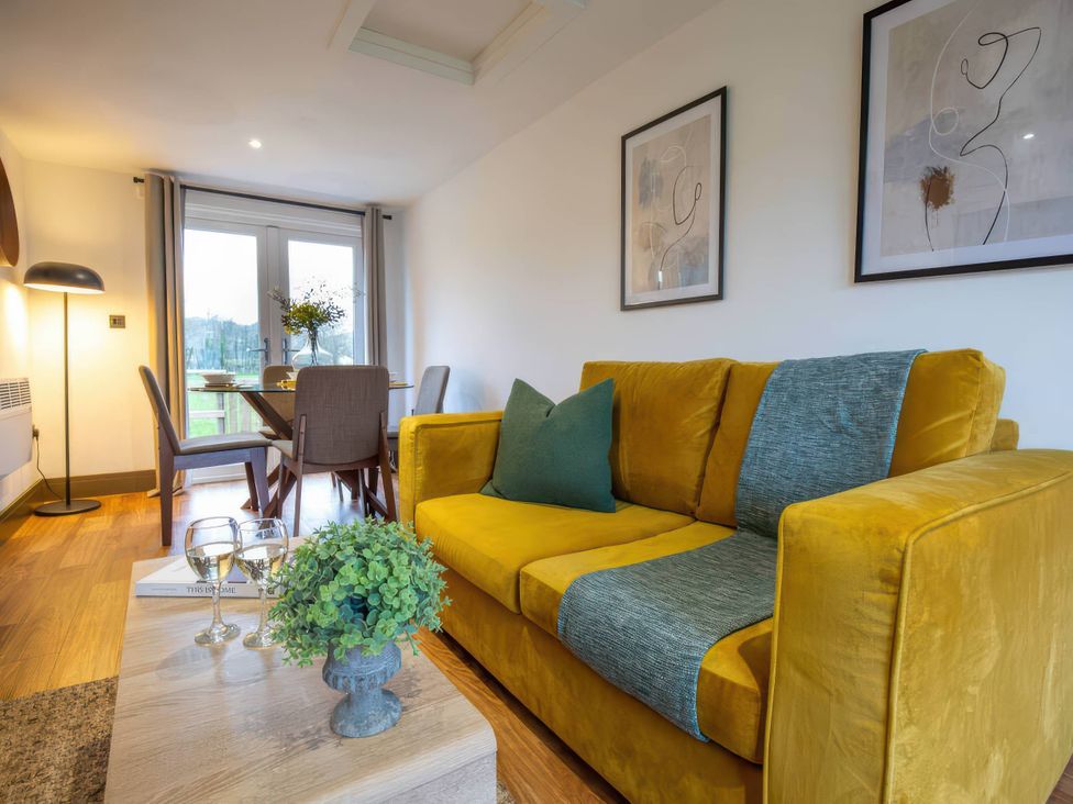 A living room with a yellow sofa and dining area at Silver Birch Cottage in Llanrwst