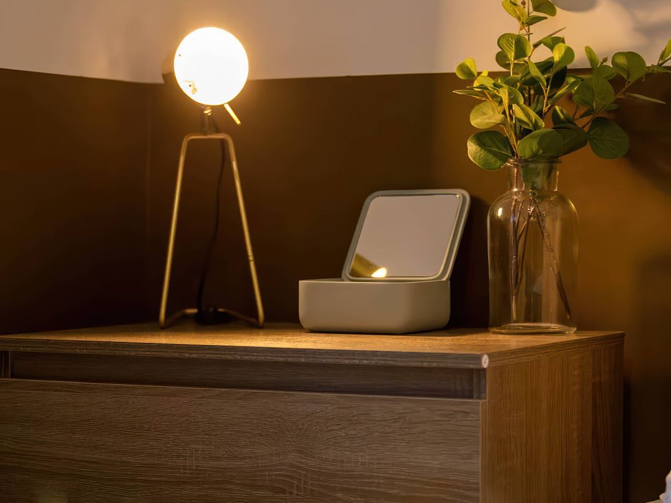A table with a lamp, mirror, and vase at Silver Birch Cottage in Llanrwst
