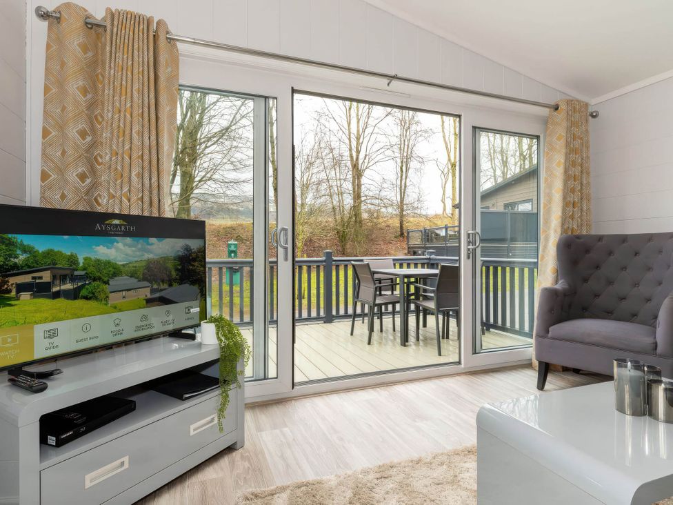 A living room with a sofa and TV leading to a deck at The Falls in Leyburn