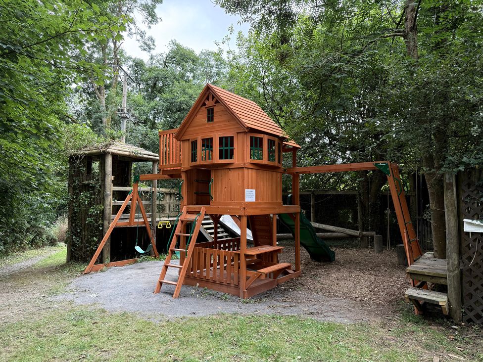 A playhouse with slide and swings in an outdoor play area at Teifi Newcastle Emlyn