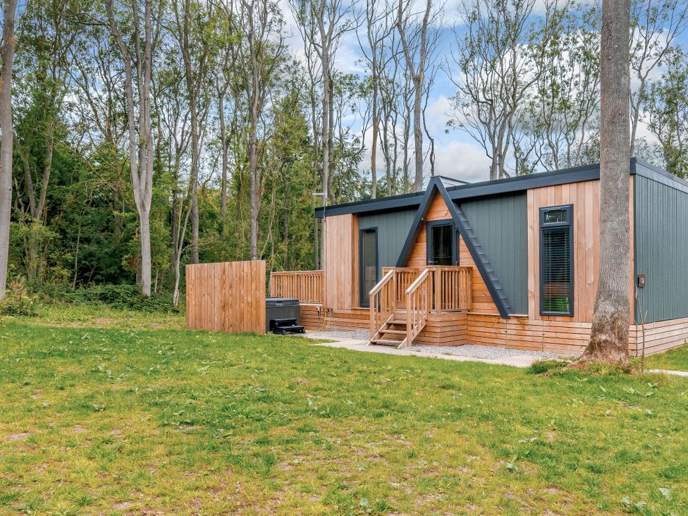 A house with a deck and hot tub surrounded by trees at Tennyson Spa in Louth