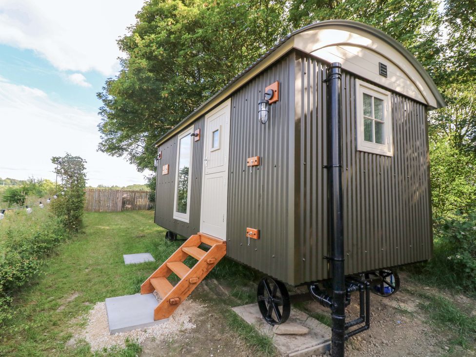 A shepherd's hut with stairs and a doorway in a grassy area at Kingfisher Hut