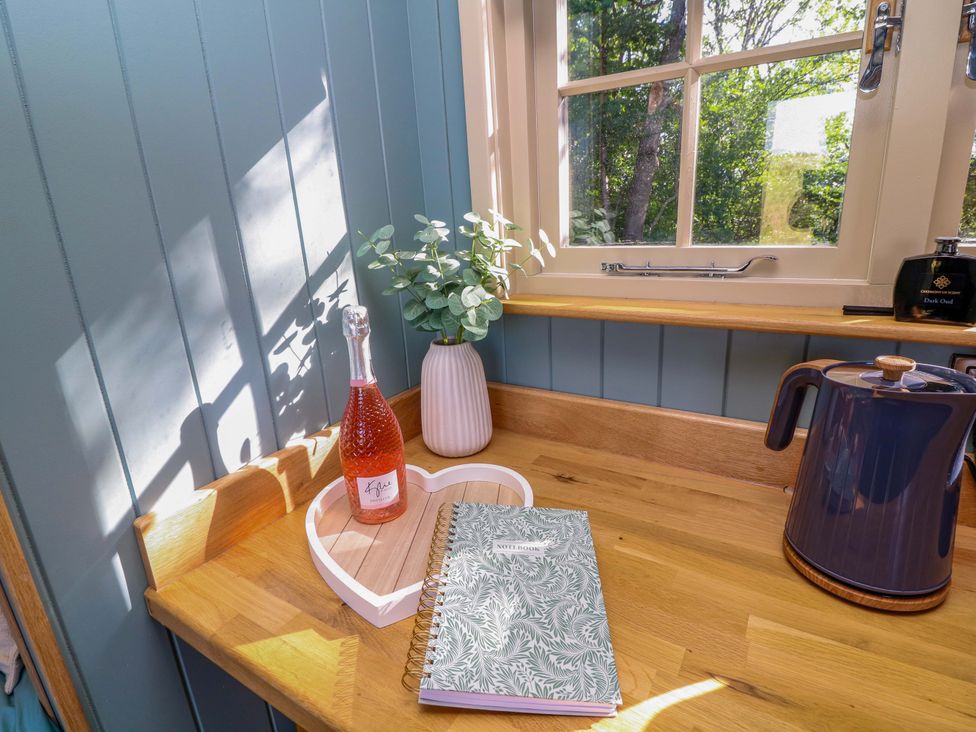 A kitchen countertop with a bottle, plant, notebook, heart-shaped tray, and kettle at Kingfisher Hut