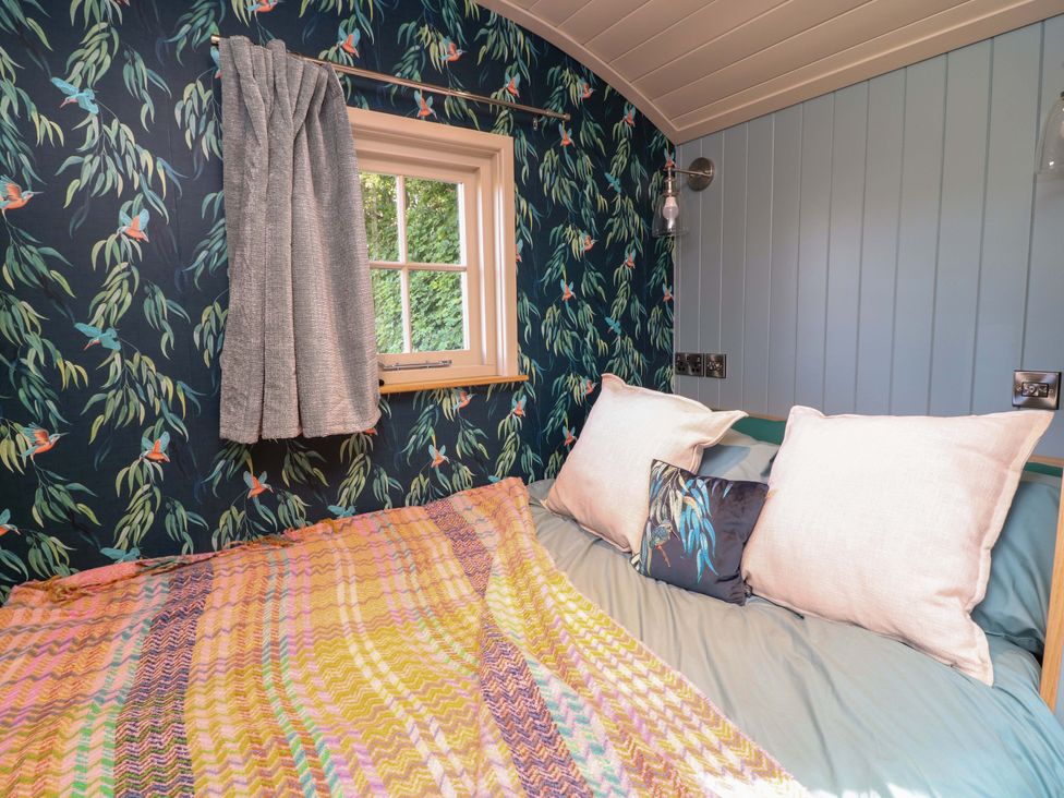 A bedroom with a bed, pillows, and a window at Kingfisher Hut