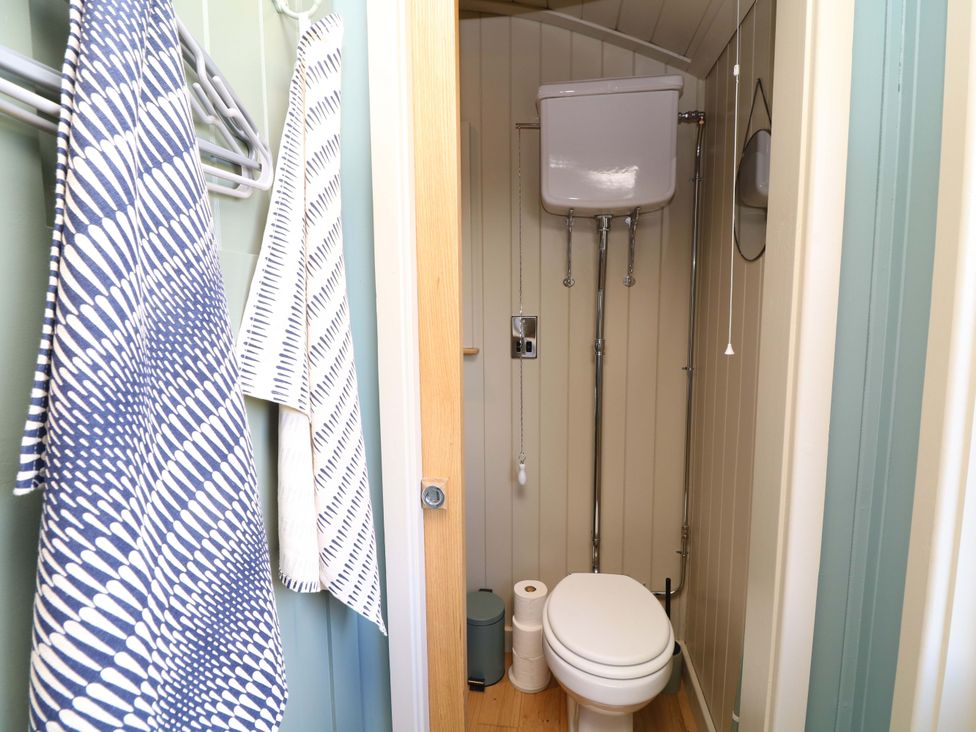 A bathroom with a toilet and towels hanging in Kingfisher Hut