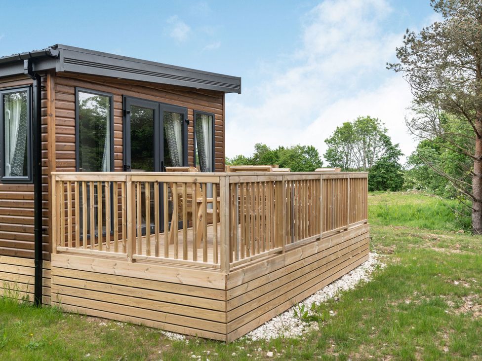 A wooden deck with a cabin surrounded by grass and trees at Caistor Spa in Louth