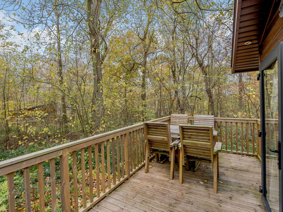 A deck with a wooden table and chairs surrounded by trees at Alford Spa in Louth