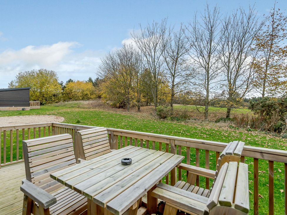 A wooden table and chairs on a deck overlooking a grassy area with trees at The Kinder Spa in Louth