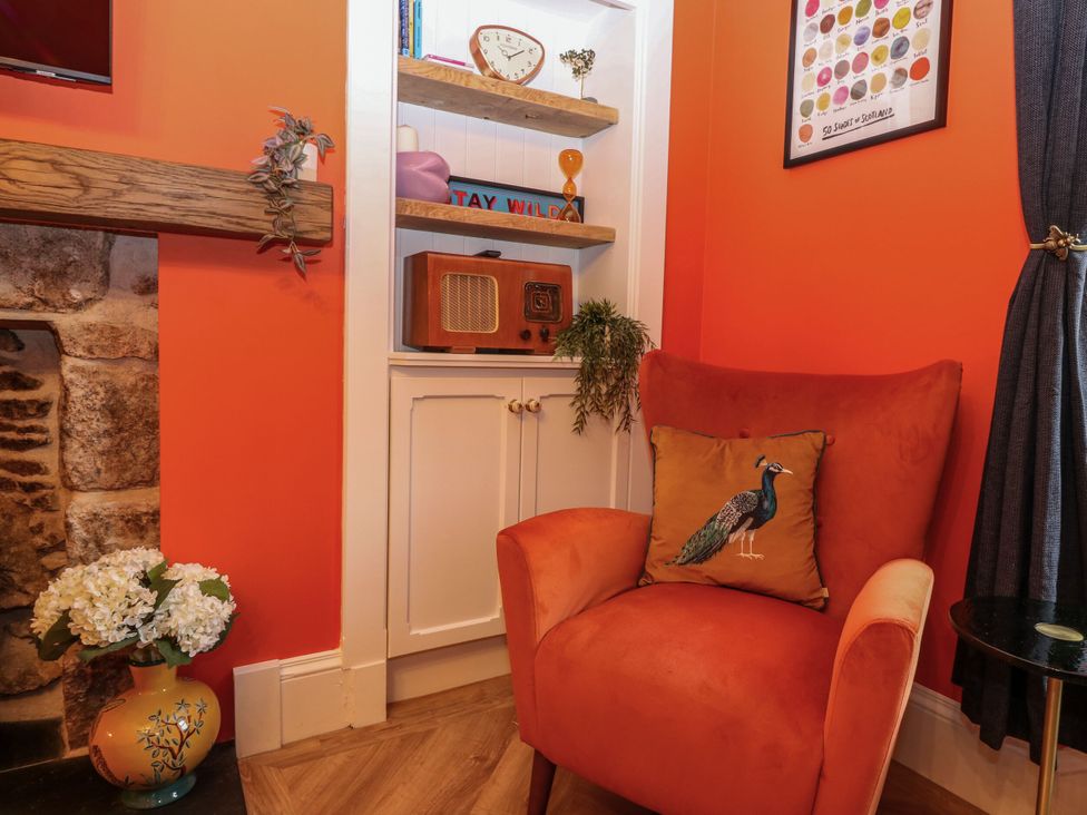 A snug with an armchair and a shelf displaying a clock and radio at Lindean in Ballater