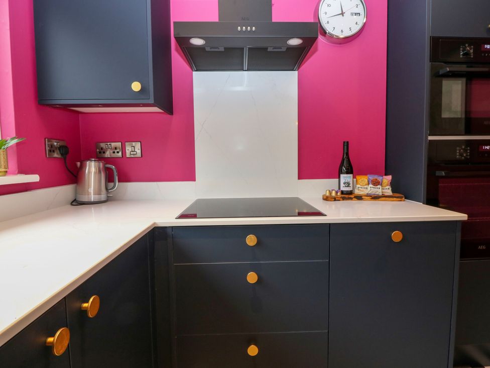 A kitchen with a kettle, cooker, wine bottle, and clock at Lindean in Ballater