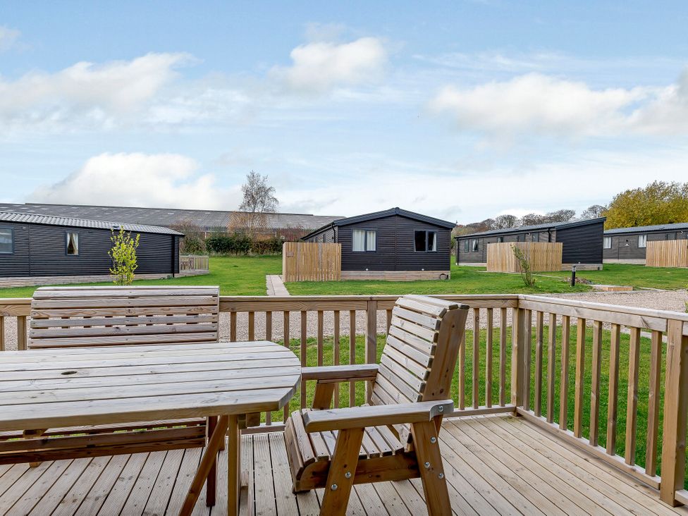 A wooden table and chair on a deck overlooking cabins at Elsham Lodge (Pet) in Louth