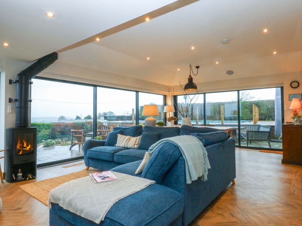 A living room with a wood stove and large windows at Bryn Mor Cottage in Mynytho near Llanbedrog