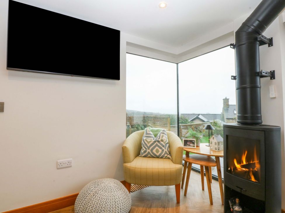 A living room with a TV, armchair, wood stove, and side table at Bryn Mor Cottage Mynytho near Llanbedrog