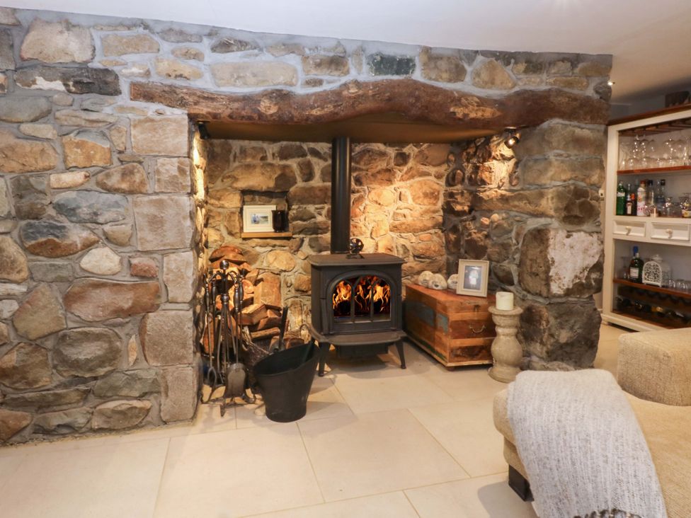 A living room with a wood stove and stone wall at Bryn Mor Cottage Mynytho near Llanbedrog